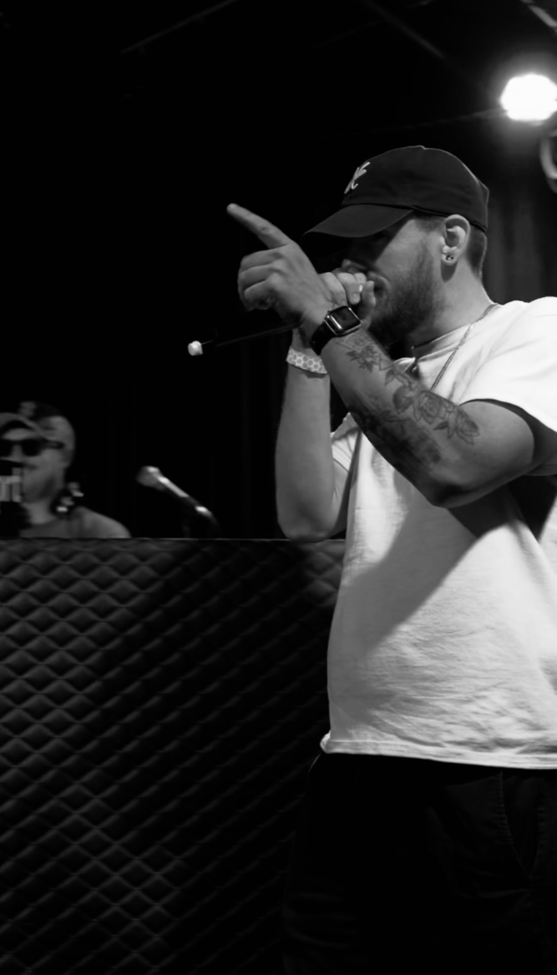 Mr. Ok performing into a microphone on stage, wearing a cap with the handwritten OK logo