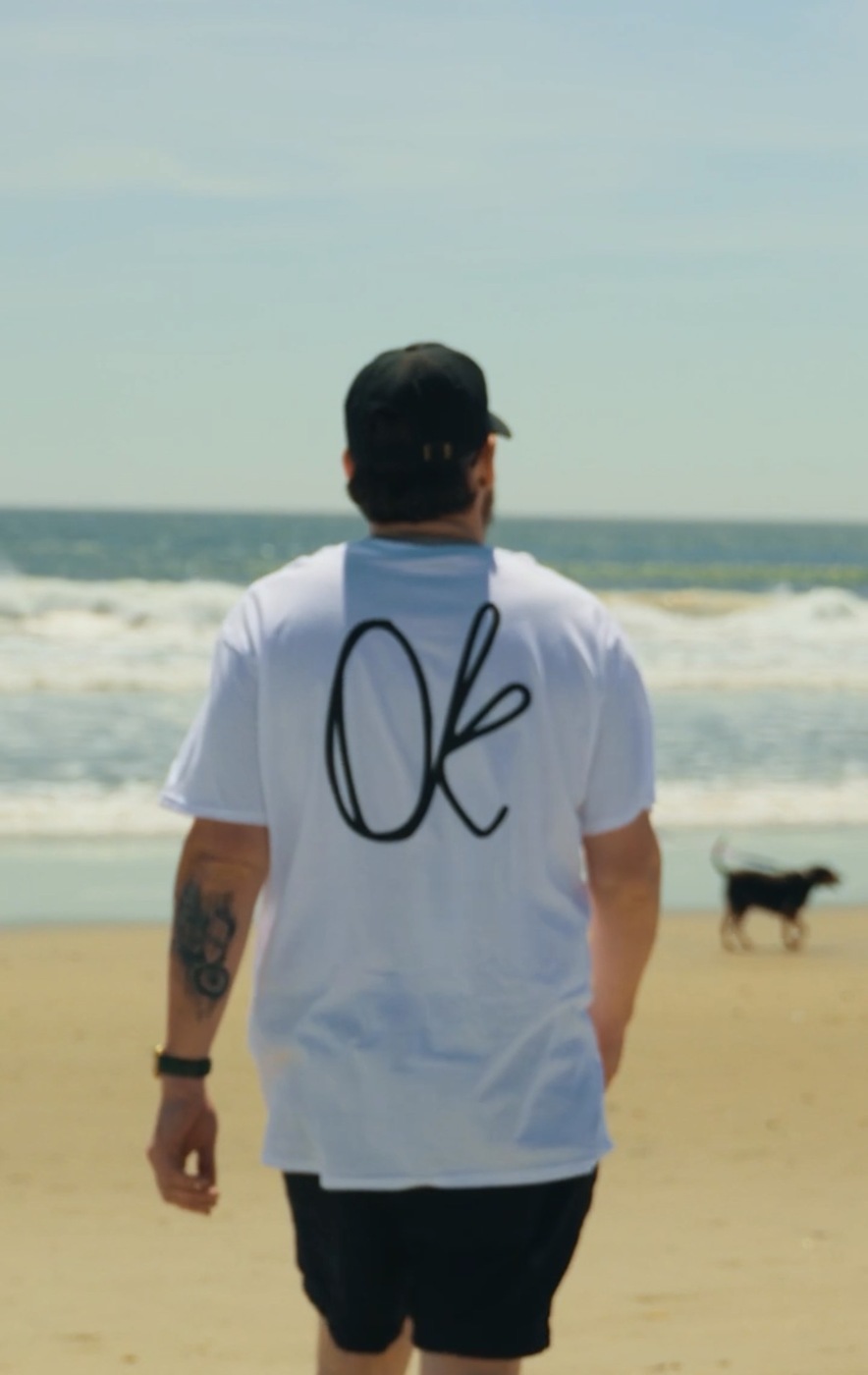 Mr. Ok on the beach wearing the white Original Kreations T-shirt with the OK logo on the back